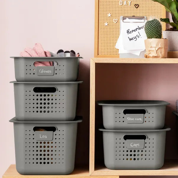 Stack of gray storage baskets labeled with various items on a wooden shelf.