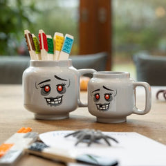 Two grey mugs with cartoon faces on a table with small tools and items.