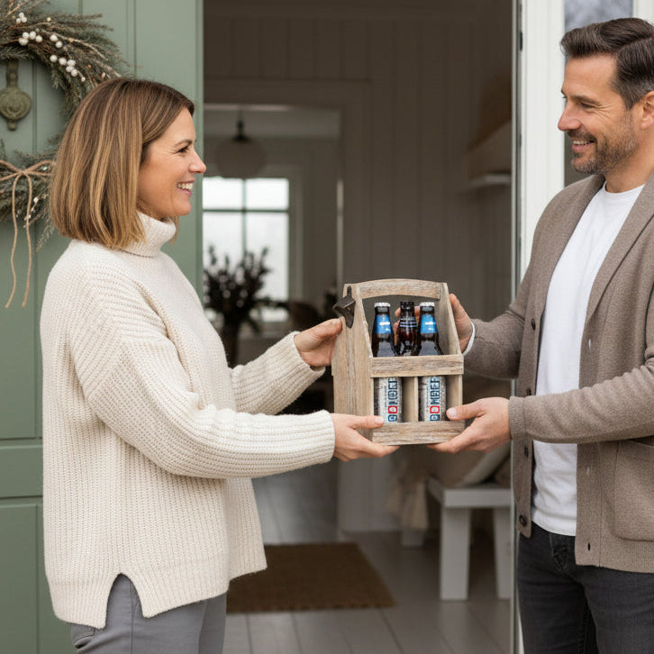 Man and woman exchanging a gift box with drinks at a front door.