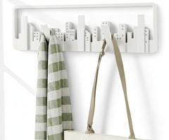 White wall hook with cityscape design holding a green checkered towel and beige strap against a white background