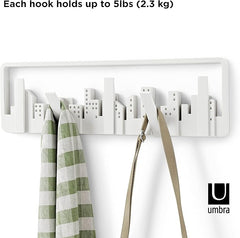 White wall hook with cityscape design holding a green and white striped towel and a beige bag, with text indicating weight capacity and Umbra logo.