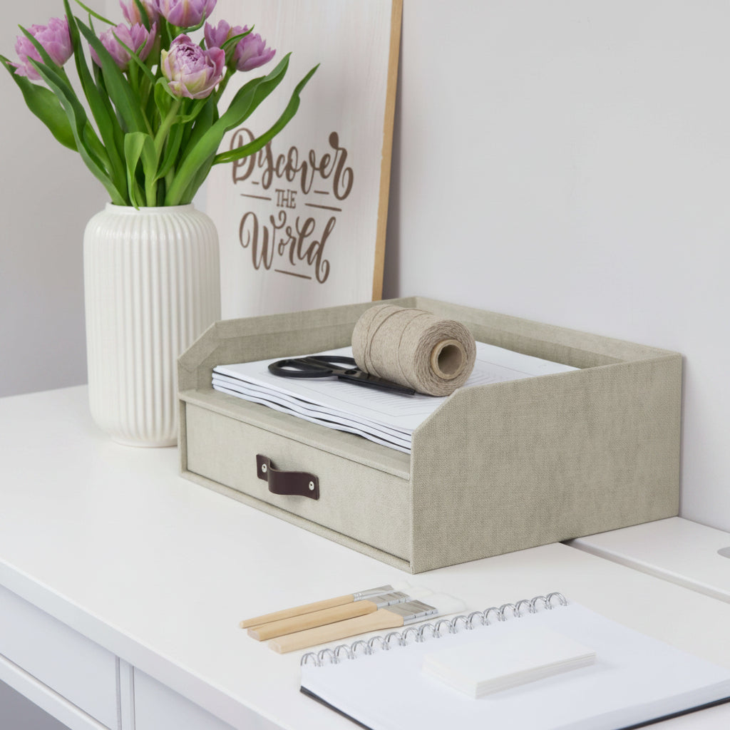 Beige desk organizer with stationery items on a white desk with flowers and decor.