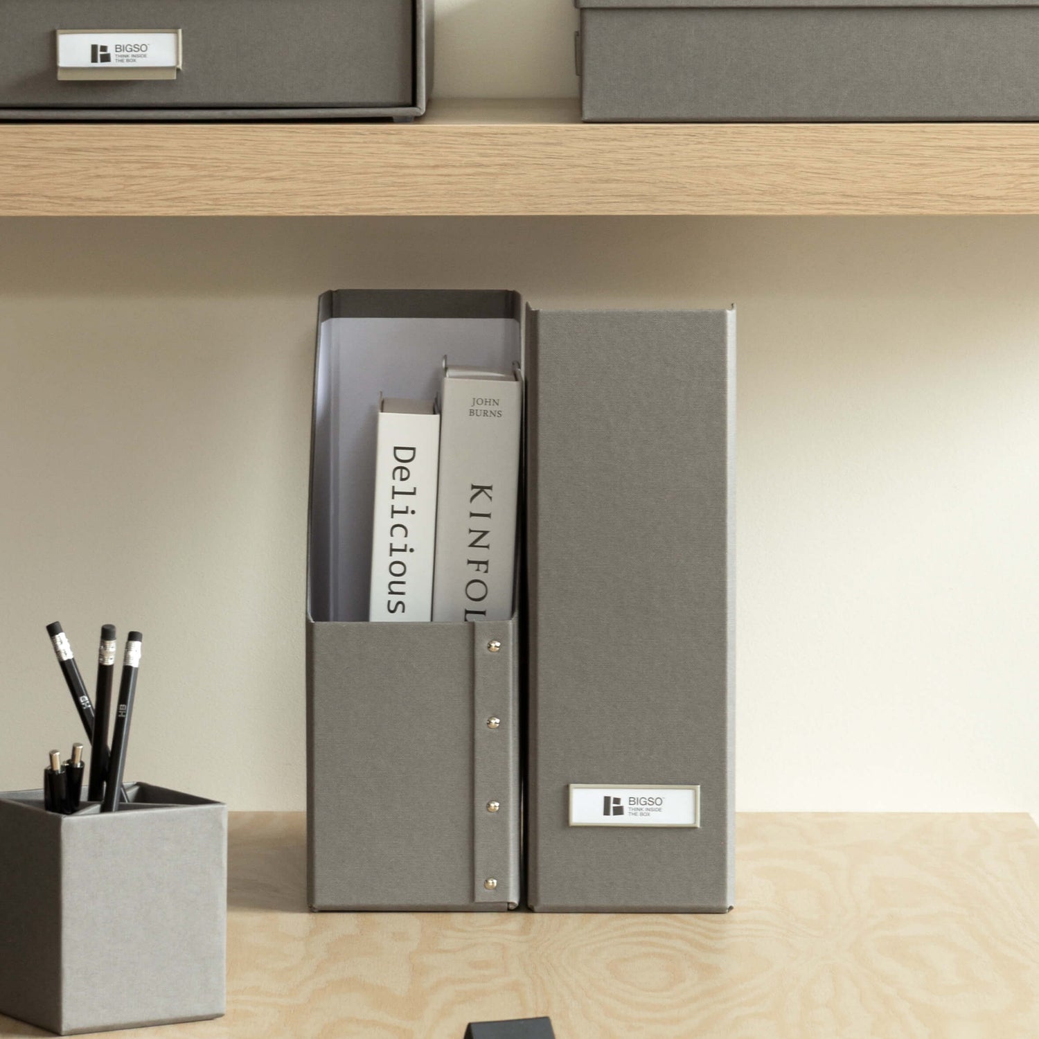 Gray office supplies including folders, a pen holder, and a notepad on a wooden shelf.