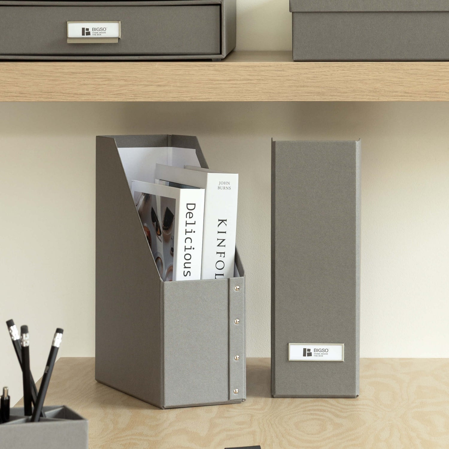 Gray office supplies including folders, a pen holder, and stationery on a wooden shelf.