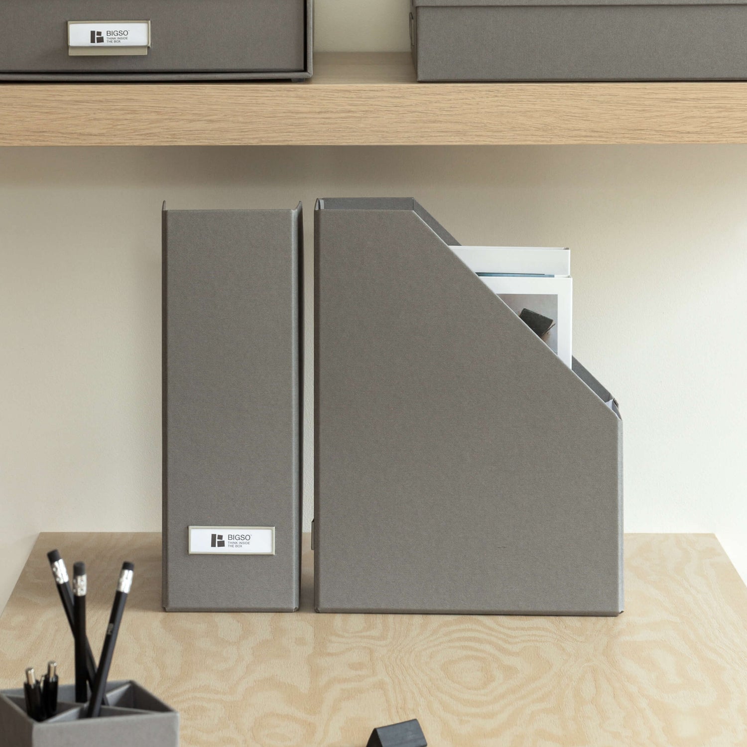 Gray office supplies including folders, a pen holder, and a notepad on a wooden desk.