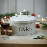White cake storage tin with 'CAKE' text on a wooden surface