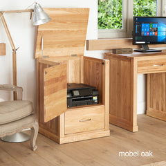 Wooden desk with open cabinet revealing a printer, lamp, and chair in a room with a window.