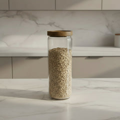 Three glass jars with wooden lids containing oats, pasta, and coffee beans on a kitchen counter.