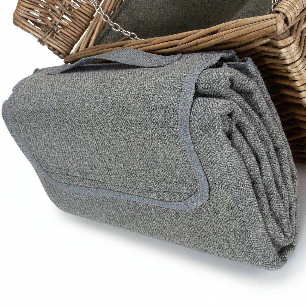Folded green picnic blanket with gray trim on a white surface next to a wicker basket.