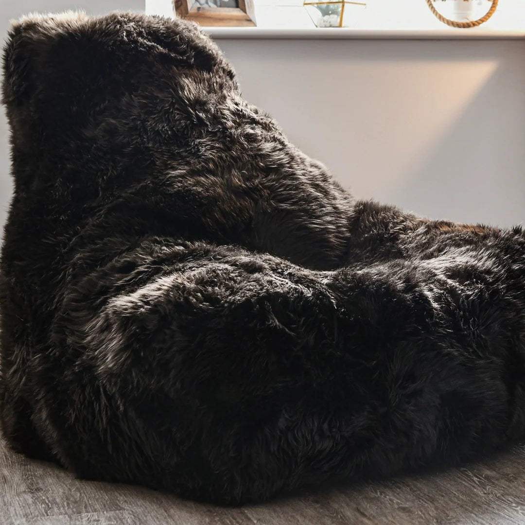 Fluffy black bean bag chair in a room with a plant and wooden cabinet.