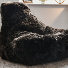 Fluffy black bean bag chair in a room with a plant and wooden cabinet.