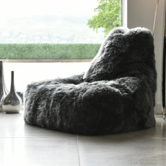 Gray fuzzy bean bag chair in a room with large windows and decorative vases.
