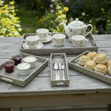 Tea set with teapot, cups, and biscuits on a wooden table outdoors.