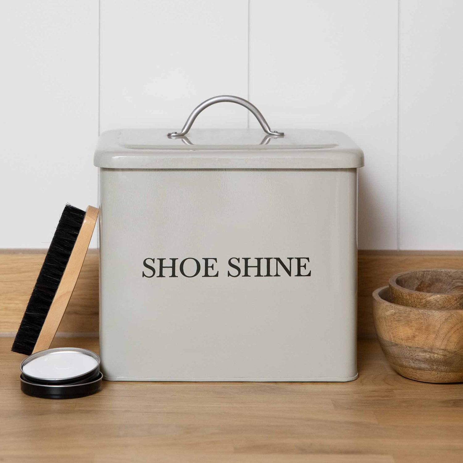 Clay coloured  shoe shine container with a black lid on a wooden surface.