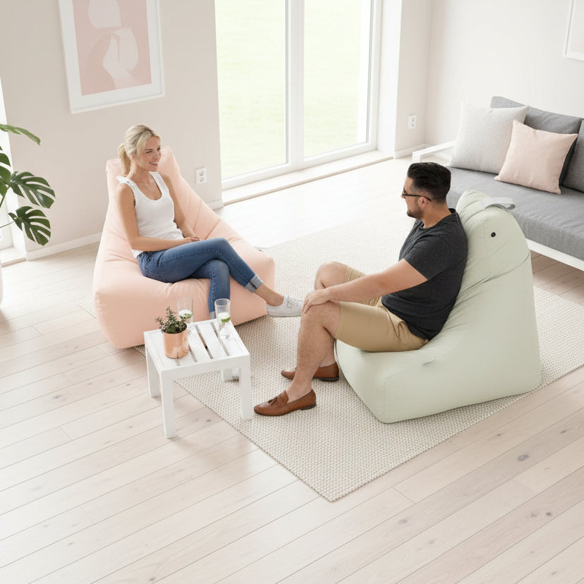 Two people sitting on bean bags on a patio with a small table and plants.