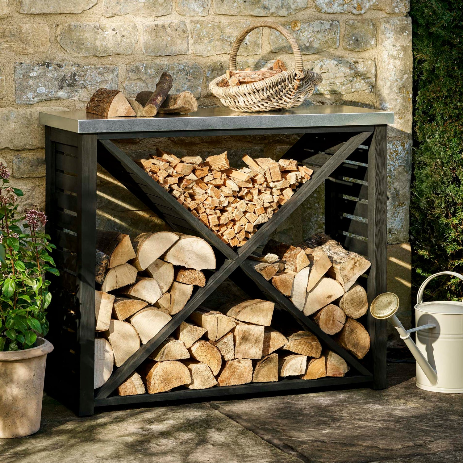 Wooden firewood storage unit against a stone wall with a basket on top.