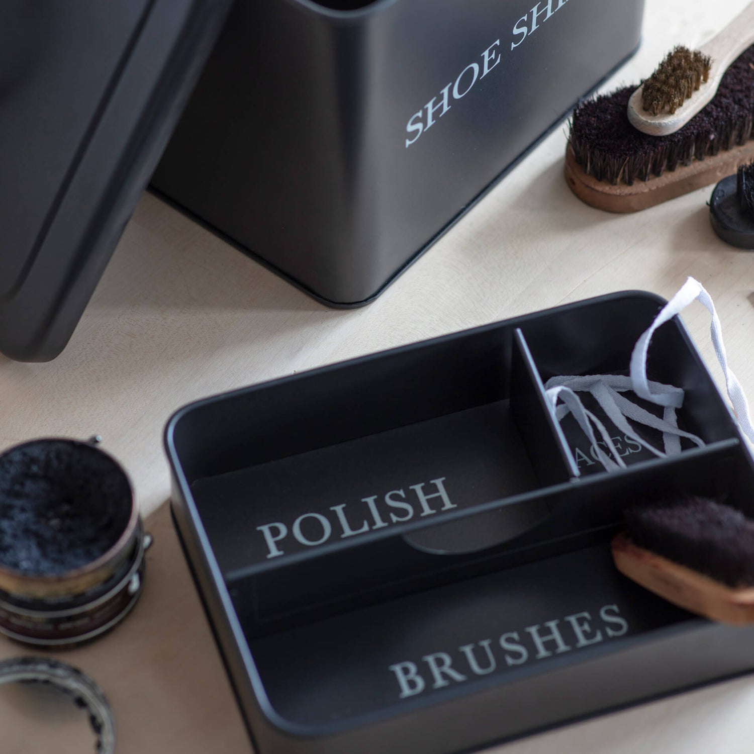 Black shoe shine kit with compartments labeled 'Polish', 'Brushes', and 'Duster' on a light surface.