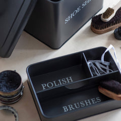 Black shoe shine kit with compartments labeled 'Polish', 'Brushes', and 'Duster' on a light surface.