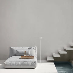 Modern indoor setting with a bed, side table, and floor lamp against a gray wall.