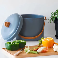 Blue compost bin with a wooden handle on a kitchen counter with food scraps.