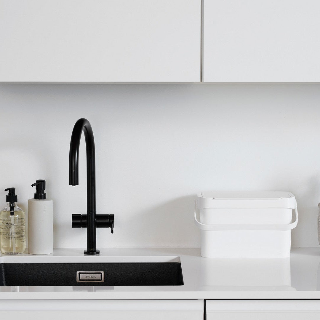 Modern kitchen with black faucet, white countertop, and decorative plants.