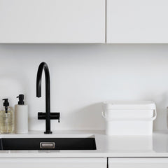 Modern kitchen with black faucet, white countertop, and decorative plants.