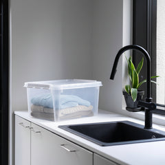 Clear storage container with folded clothes on a kitchen counter next to a sink.