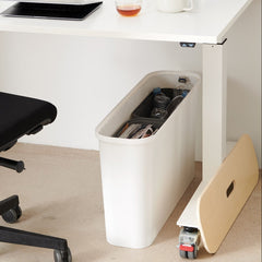 Black office chair next to a white desk with a trash can and small table in a minimalistic office setting.