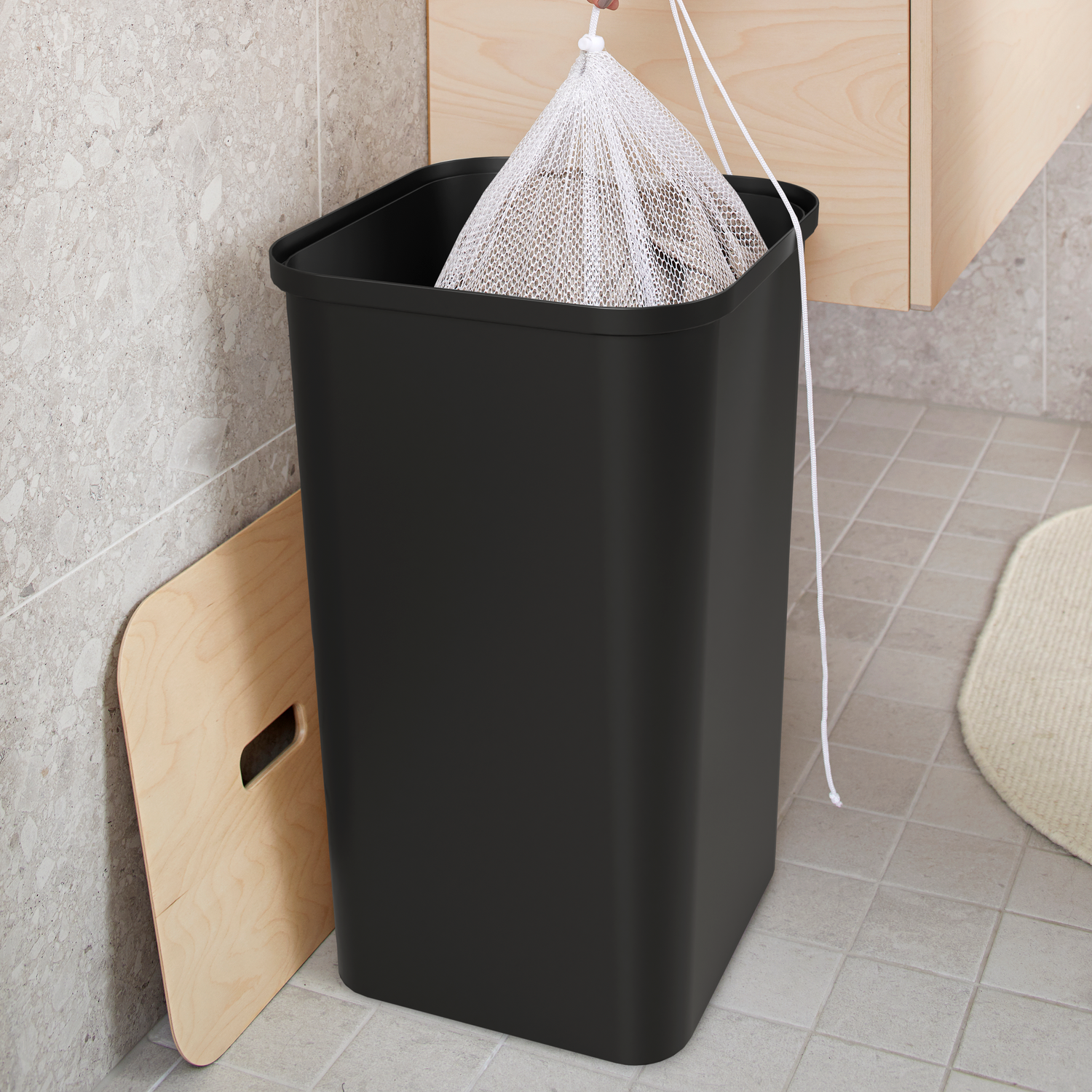 Person replacing a trash bag in a black trash can in a bathroom.