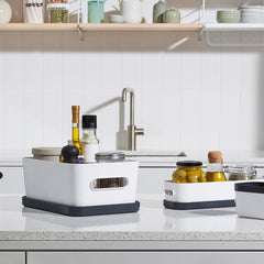 White kitchen sink with black and gray containers on a white countertop.