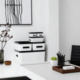 White storage boxes with black lids on a white surface, with a minimalistic background.