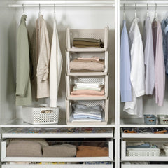A white modular closet organizer with multiple sections, shelves, and hanging rods, styled with neutral-colored clothing, folded textiles, and storage baskets.