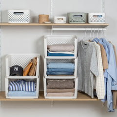 A wall-mounted floating shelf and hanger system styled with storage baskets, folded clothing, and hanging garments in a clean, minimalist room setting.