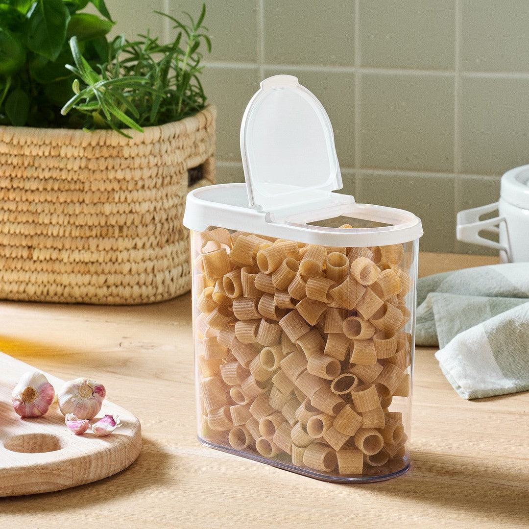 Container of pasta on a kitchen counter with a plant and other items in the background