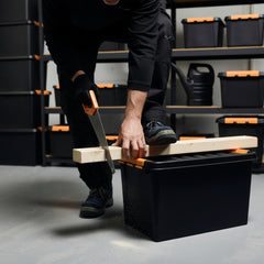Person using a saw on a wooden plank with black storage bins in the background