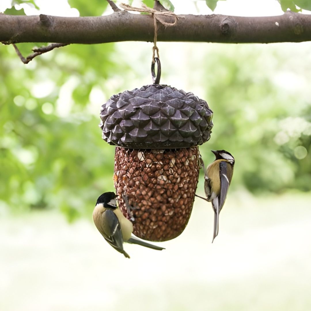 Bird feeder shaped like a pine cone with birds perched on it, hanging from a tree branch.