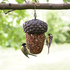 Bird feeder shaped like a pine cone with birds perched on it, hanging from a tree branch.