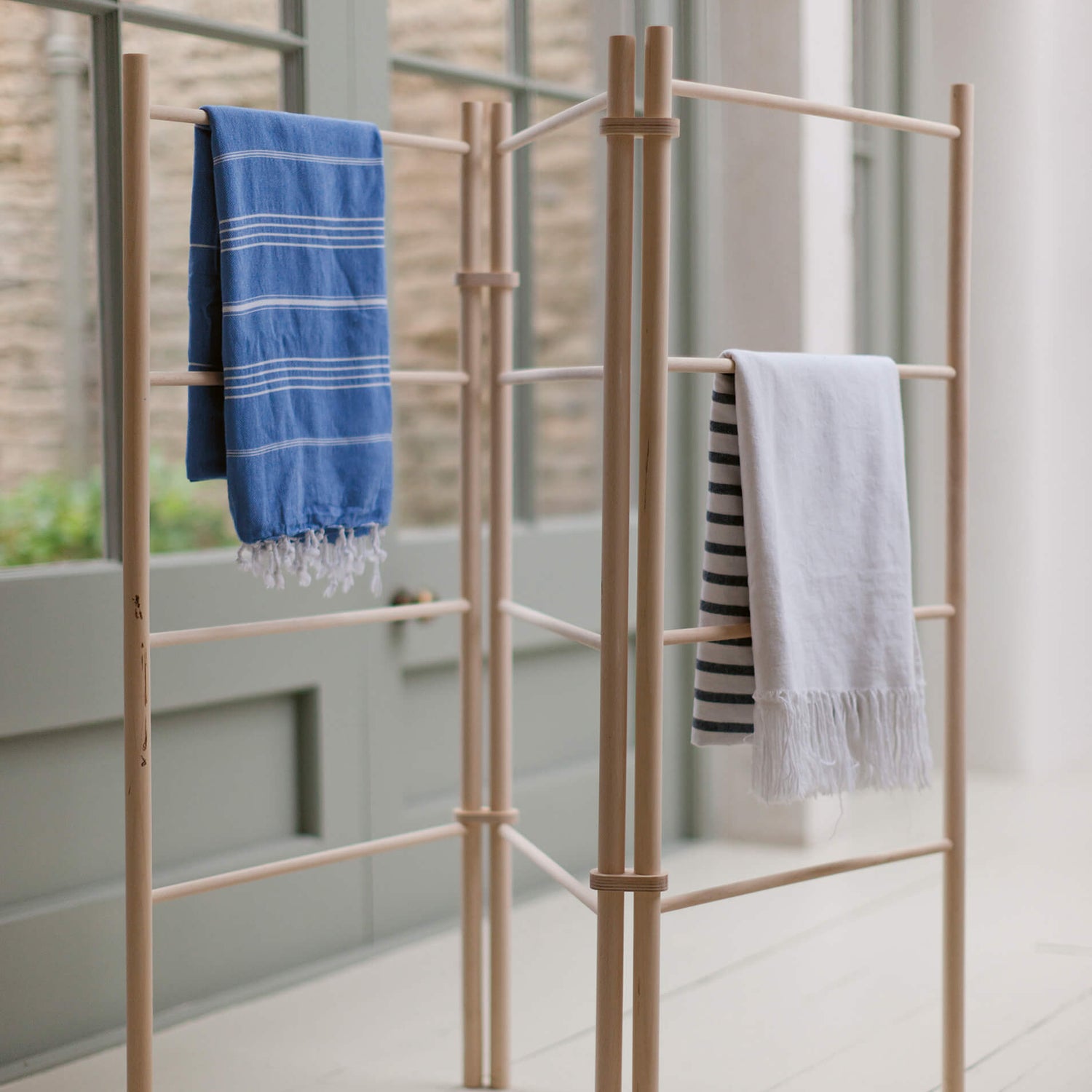 Wooden drying rack with clothes hanging on a light wooden floor.
