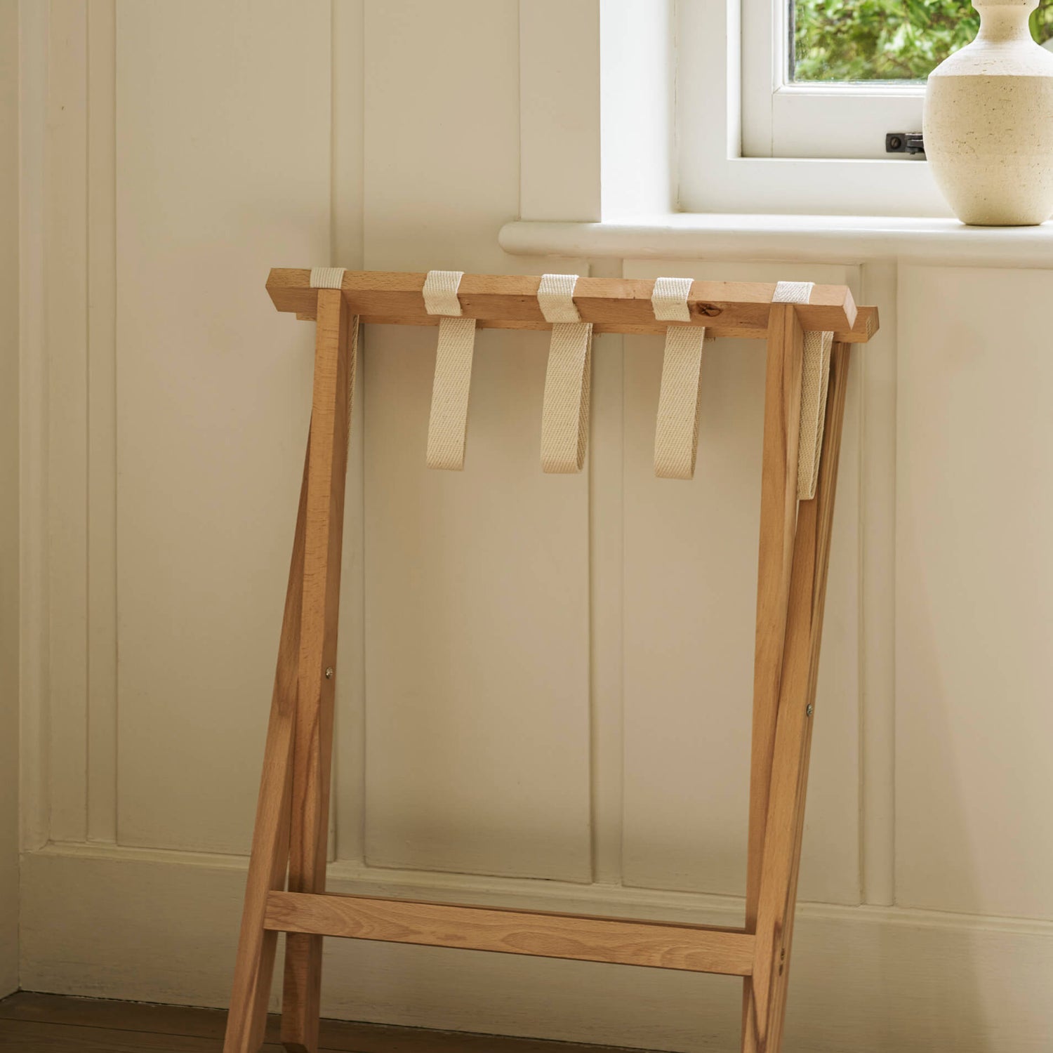 Wooden stool with straps against a neutral wall with a window in the background.