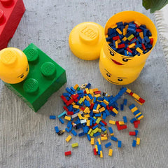 Colorful LEGO bricks spilling out of a yellow container with a face on a textured surface.