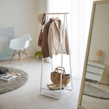 Clothing rack with coats, bags, and shoes in a room with a mirror and chair.