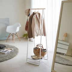 Clothing rack with coats, bags, and shoes in a room with a mirror and chair.
