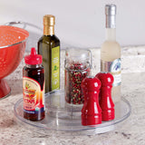 Assorted kitchen items including a bottle of balsamic vinegar, olive oil, and a pepper grinder on a clear tray.