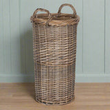 Wicker laundry basket with handles on a wooden surface against a light green wall.