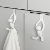 Two white hook-shaped person figures hanging on a cabinet door with a towel.
